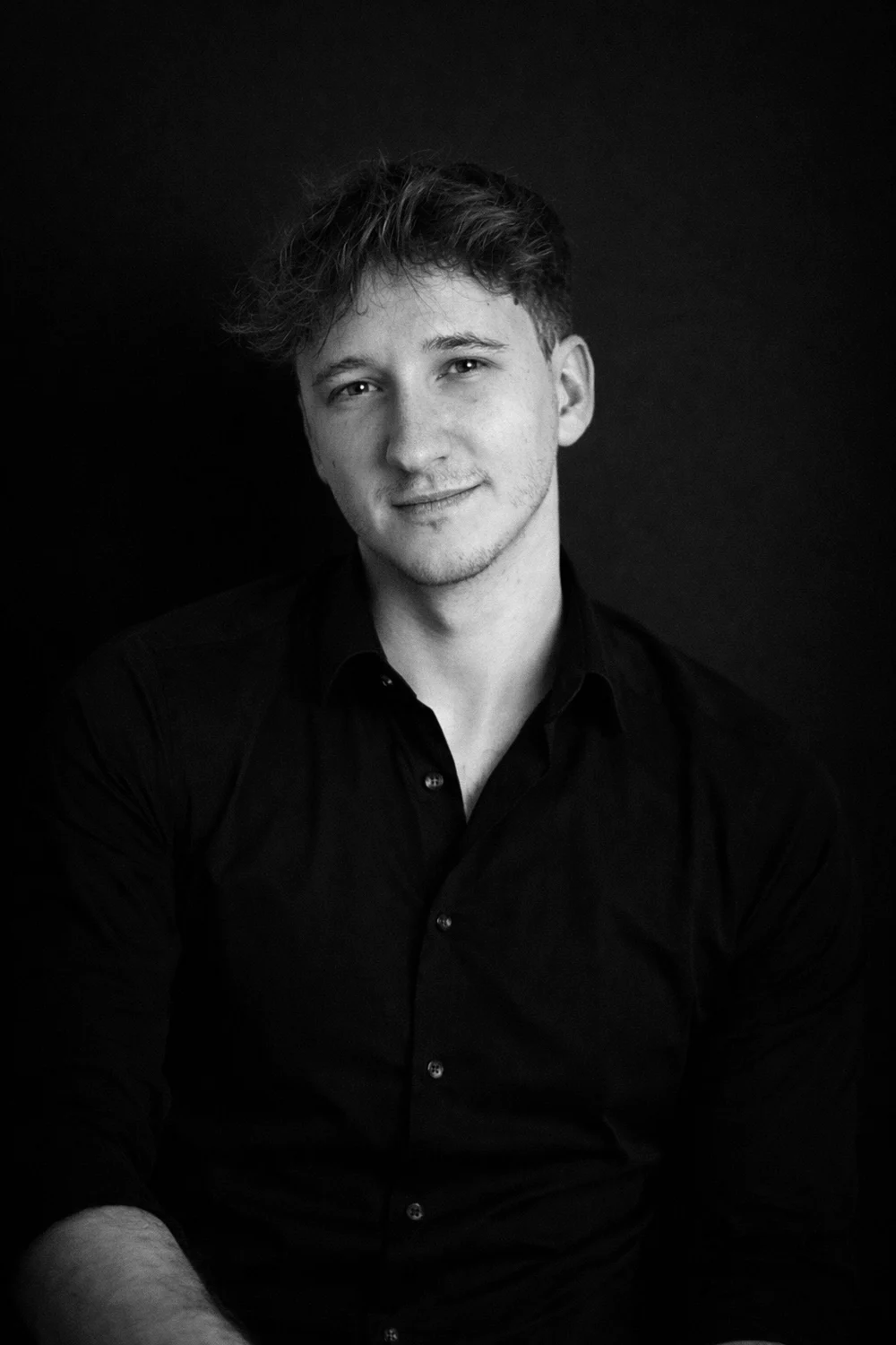 Portrait en noir et blanc de Corentin Lambert, chemise noire, fond sombre.